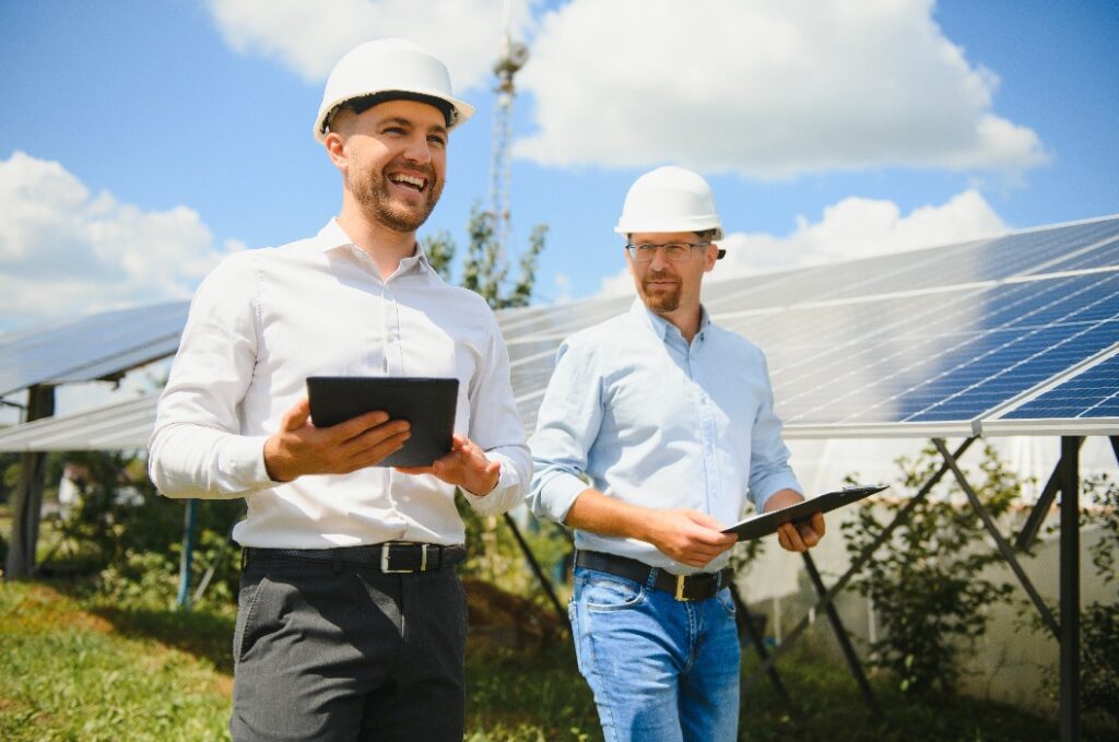 2 Männer mit Helmen lachen vor Solarmodulen